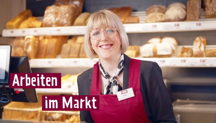 Frau steht hinter einer Bäckertheke und lächelt in die Kamera.