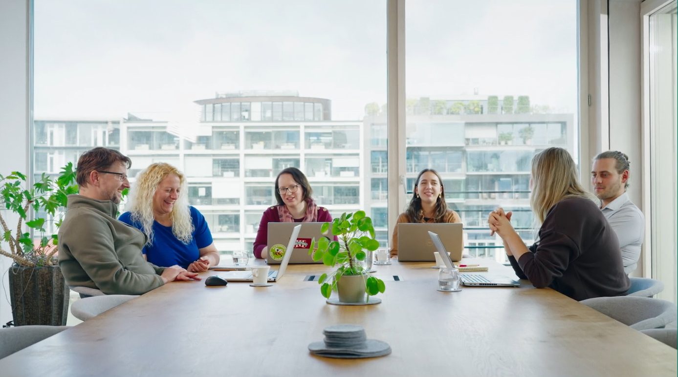 Menschen sitzen in einem hellen Meeting-Raum an einem großen Tisch.